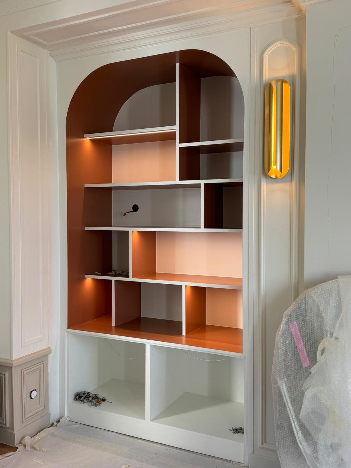 Bibliothèque sur mesure en arche, étagères laquées terracotta et éclairage intégré