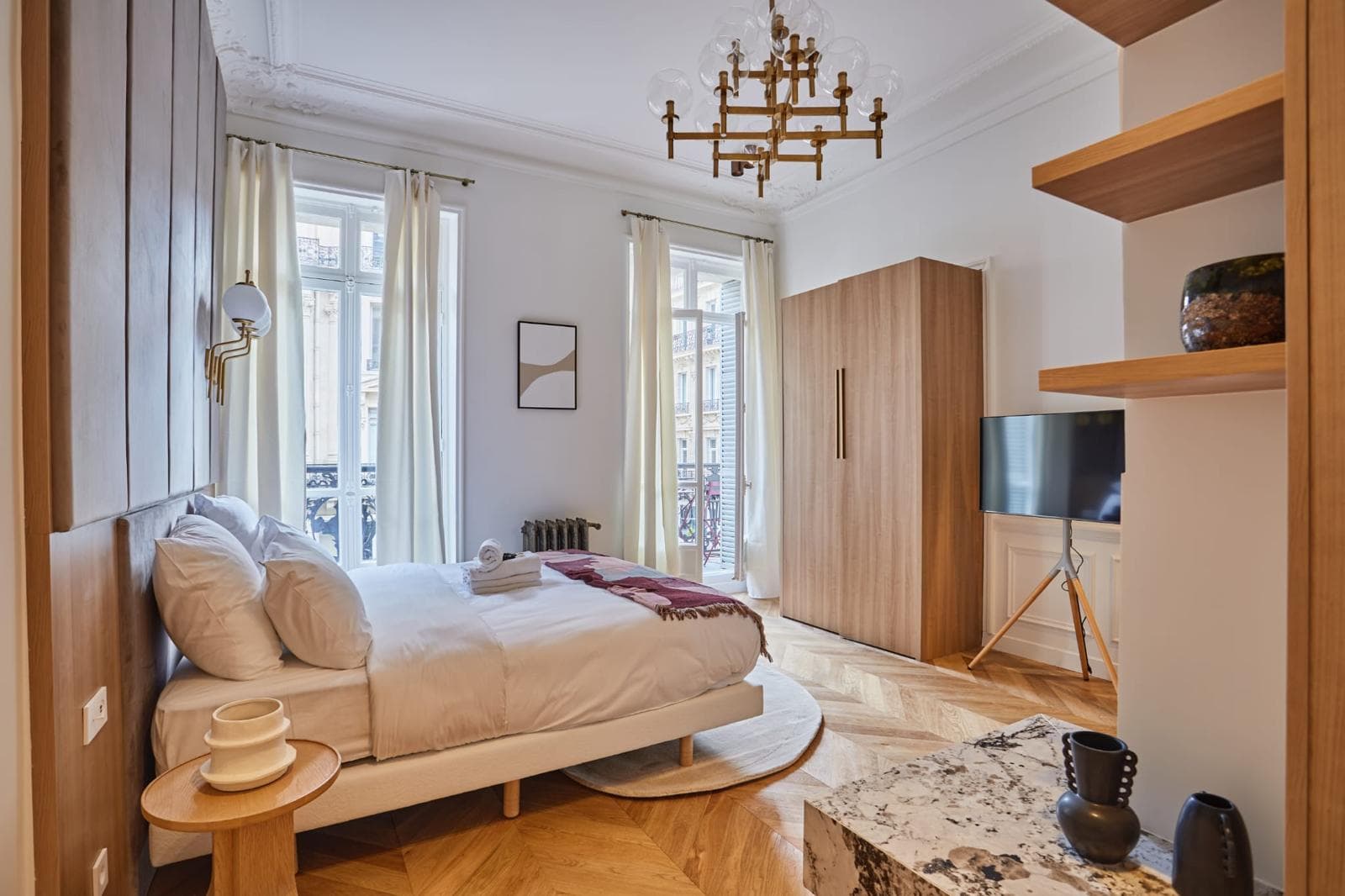 Chambre haussmannienne avec lustre, armoire en bois et parquet en chevron
