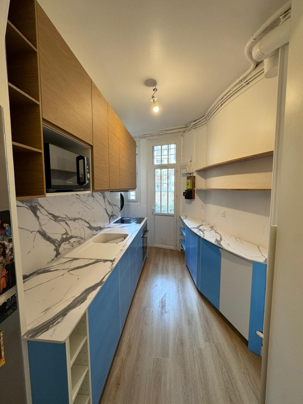 Cuisine en longueur aux façades bleues, plan de travail et crédence effet marbre