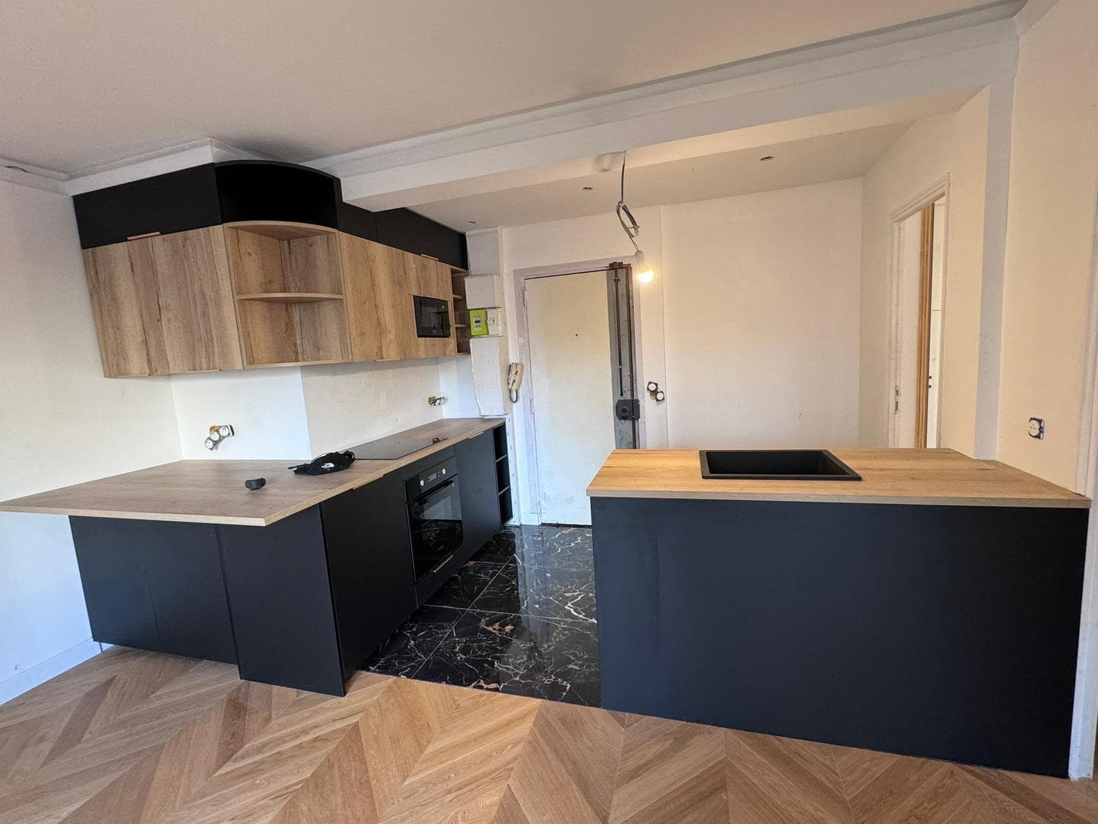Cuisine ouverte noire avec îlot et plans de travail en bois, parquet en chevron