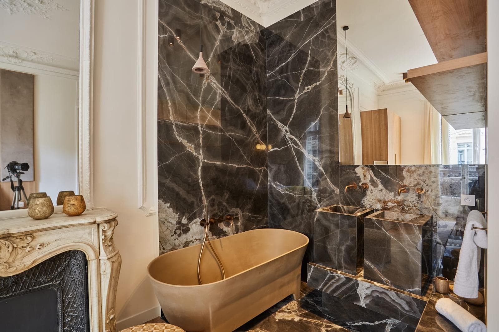 Salle de bain avec baignoire îlot cuivrée, marbre noir veiné et cheminée en marbre