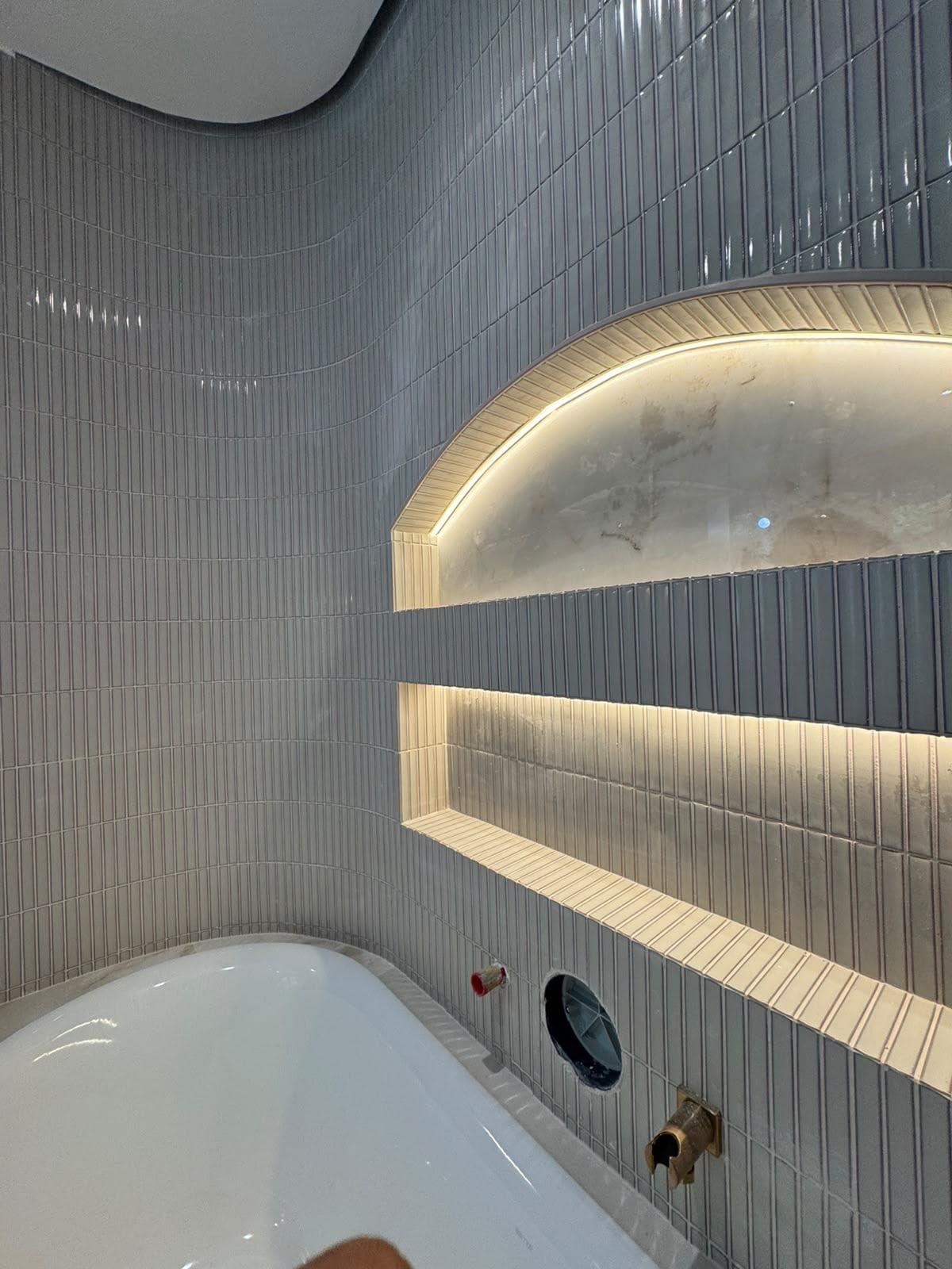 Salle de bain aux murs arrondis, niches éclairées par LED au-dessus de la baignoire