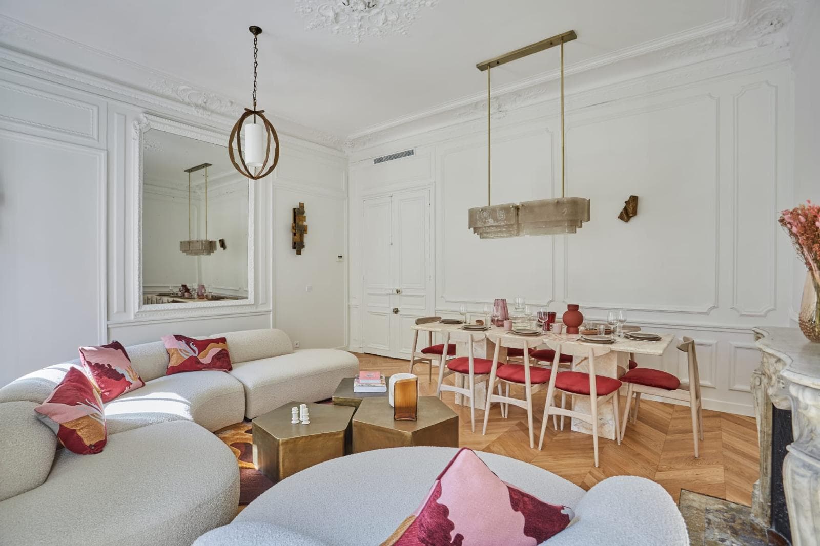 Séjour haussmannien rénové, canapé courbe, moulures et parquet en chevron ouvert sur la salle à manger