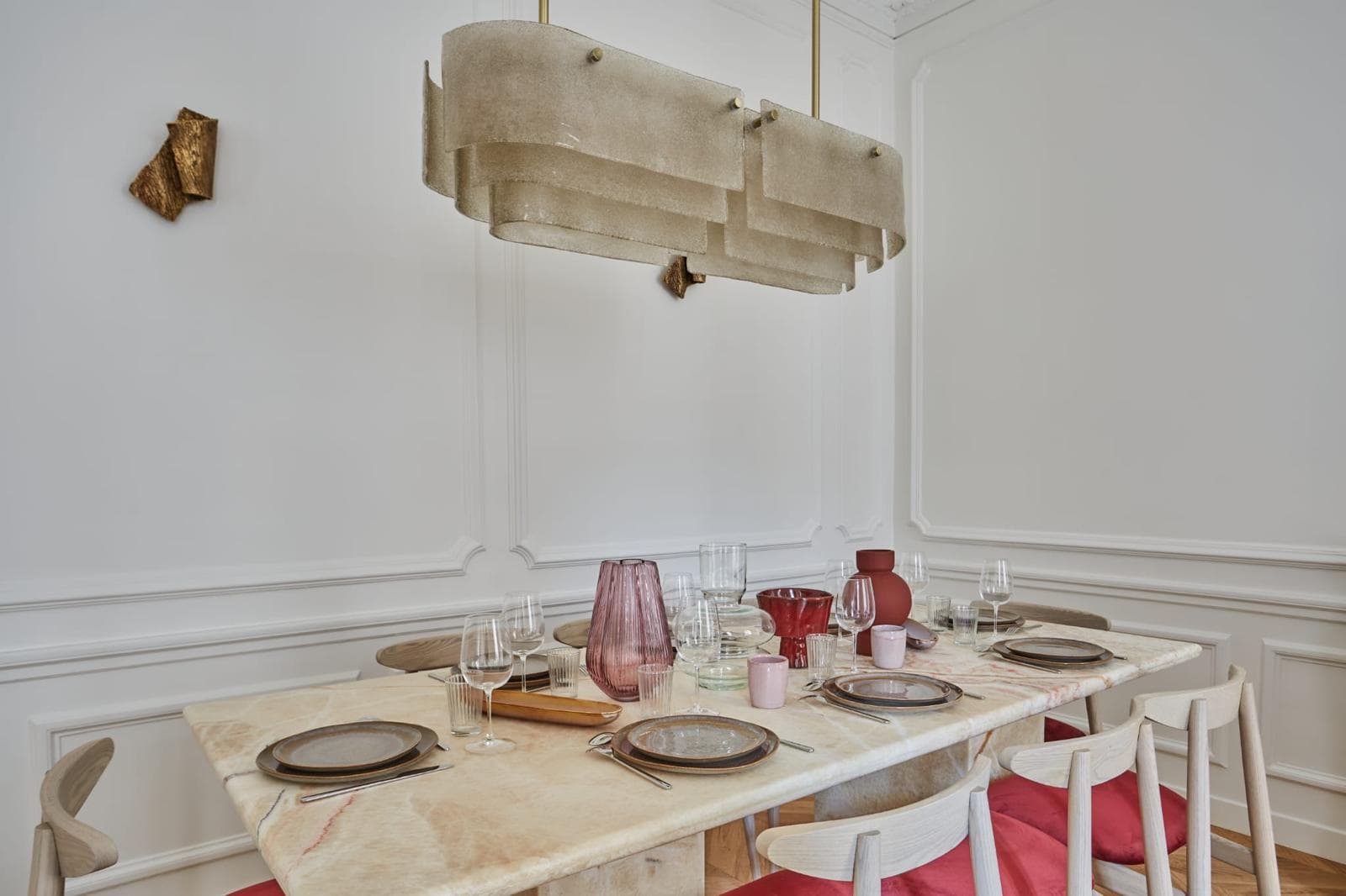 Table de salle à manger dressée sous une suspension en albâtre, murs à moulures